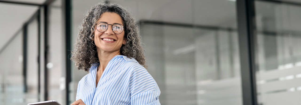 Mulher de óculos sorri e segura tablet