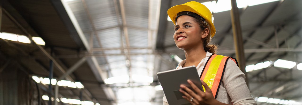 Mulher negra, de capacete, segurando um tablet e sorrindo