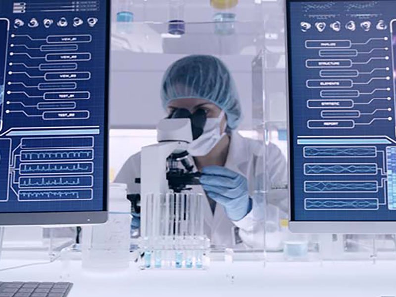 Life sciences laboratory with a scientist at work between two computer screens showing scientific data