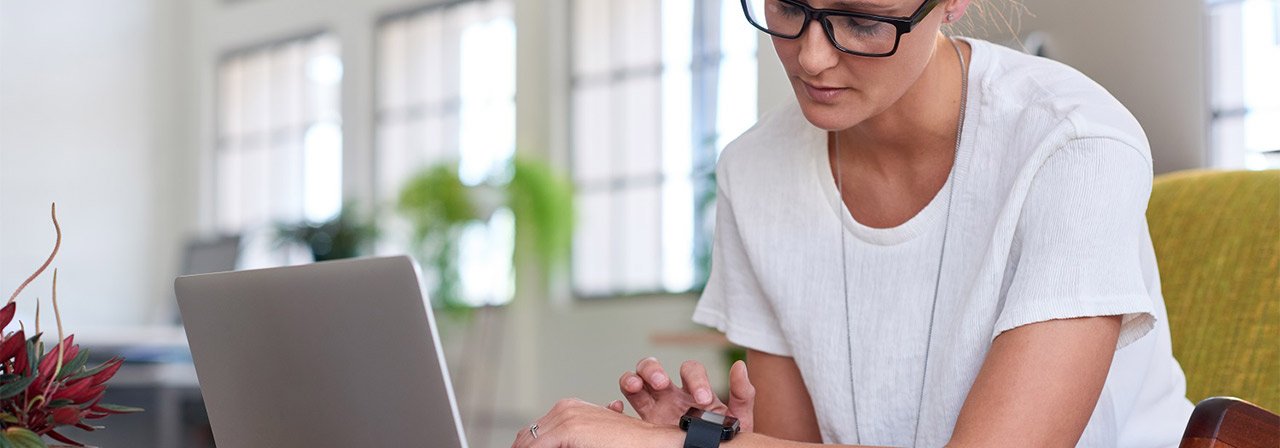 A female sitting on a chair in front of her laptop and accessing her smart watch