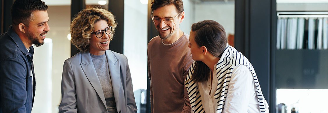 Business professionals gather around a laptop, smiling and discussing ideas, reflecting a positive and collaborative atmosphere.