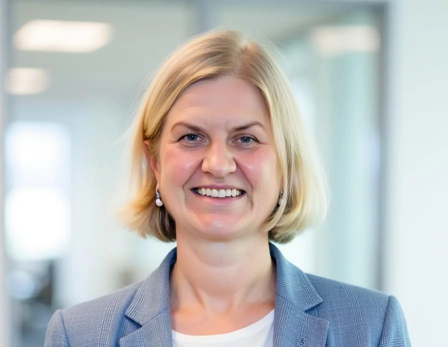 Professional in blue plaid blazer with white top smiling in bright office environment.