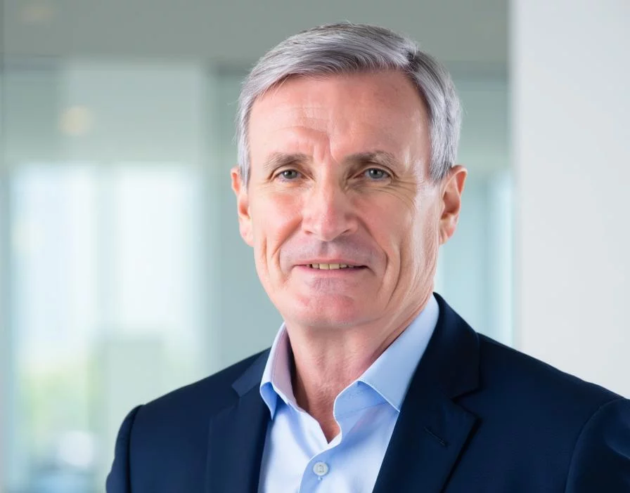 Professional with gray hair in navy suit and light blue shirt smiling against blurred office background.