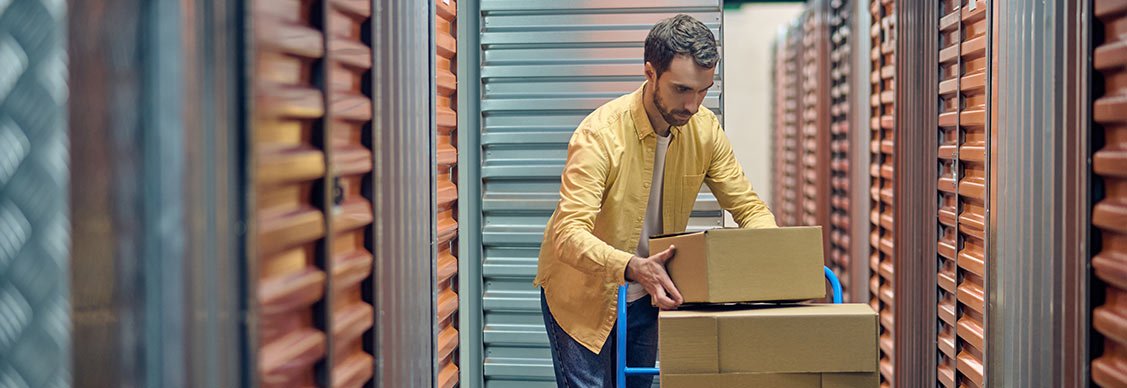 Mann lädt Kisten von einem Wagen in eine Self Storage Einheit.