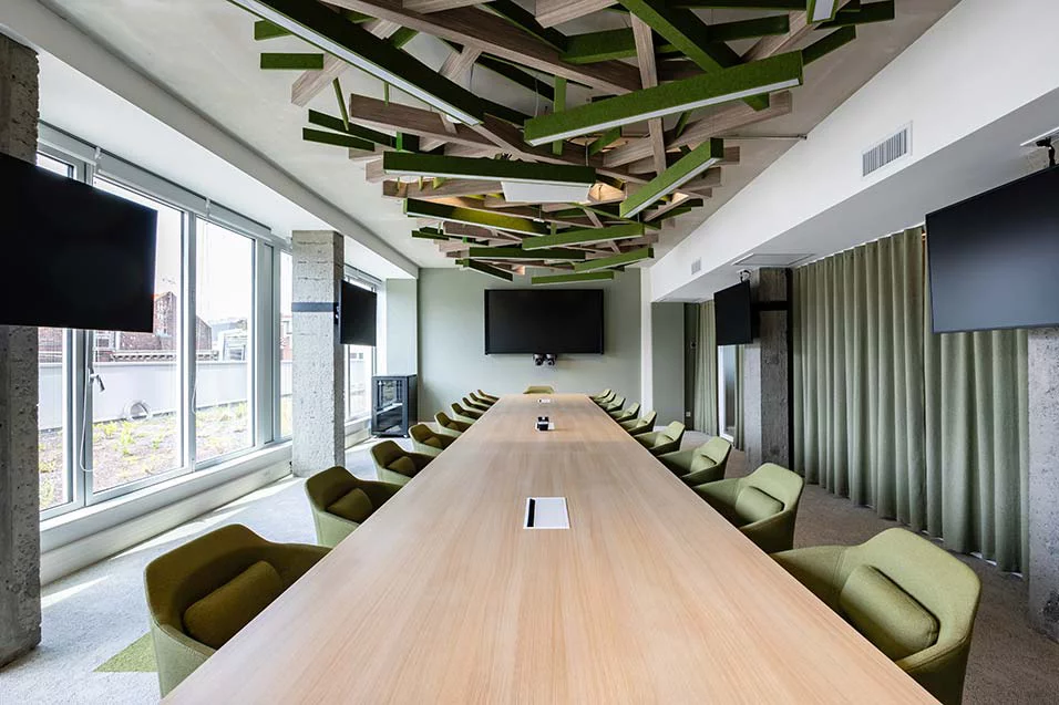 A spacious conference room with green chairs surrounding a large wooden table, designed for collaborative discussions.