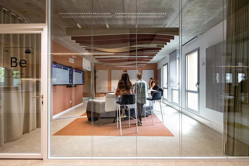 Inside a glass-walled office, a group of individuals is gathered around a table, collaborating on a project.