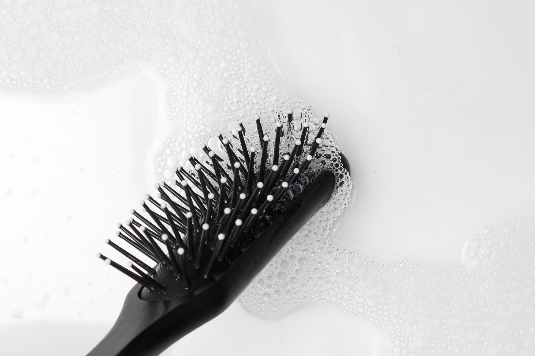 a hairbrush getting clean in water with a cleansing or clarifying shampoo