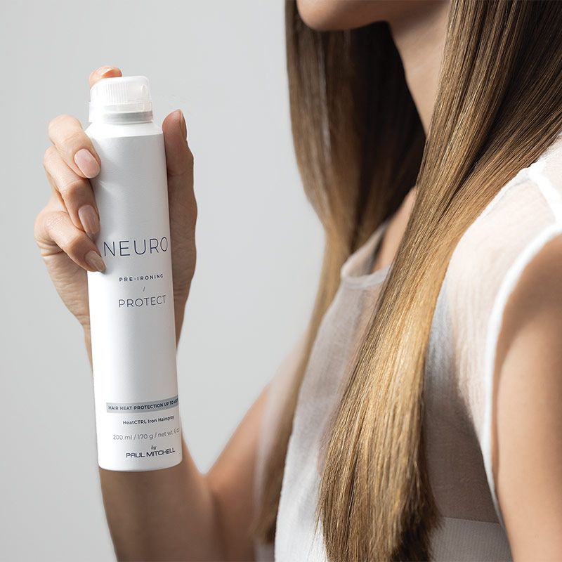 image of a woman spraying heat-protectant hairspray in her hair