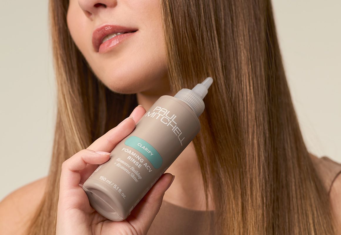 image of a model holding a bottle of Paul Mitchell Foaming ACV Rinse
