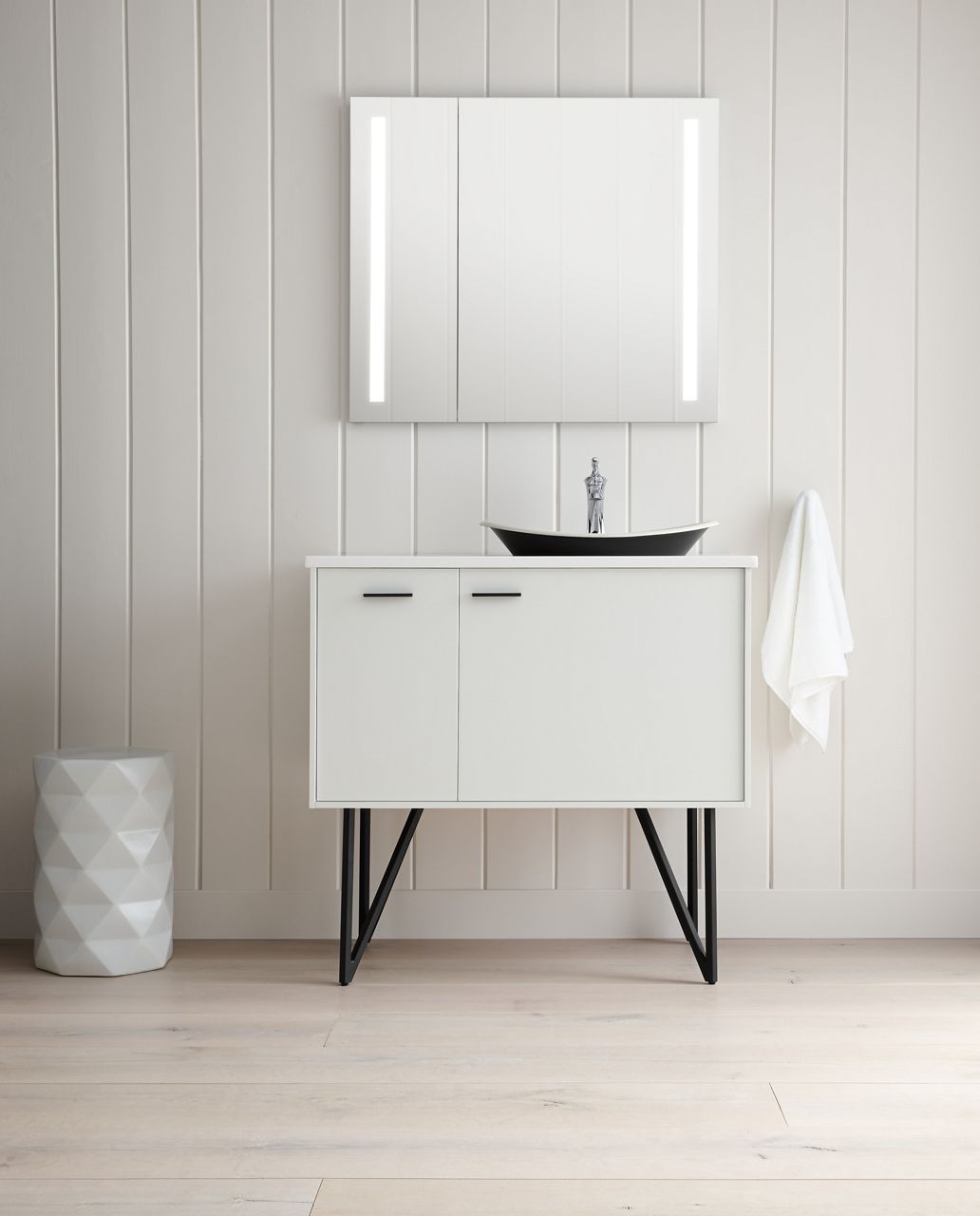 A KOHLER Verdera Lighted medicine cabinet hangs above a white vanity with fabricated metal legs and a dark vessel sink.