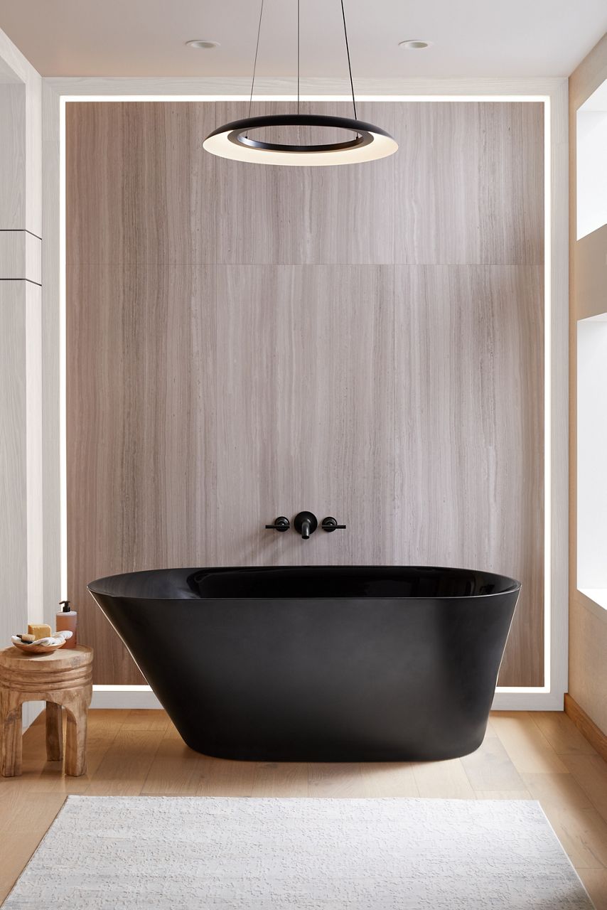 A freestanding Black Brazn Tub in a modern bathroom placed on a wood floor with beige wall and complementary black wall mounted faucet