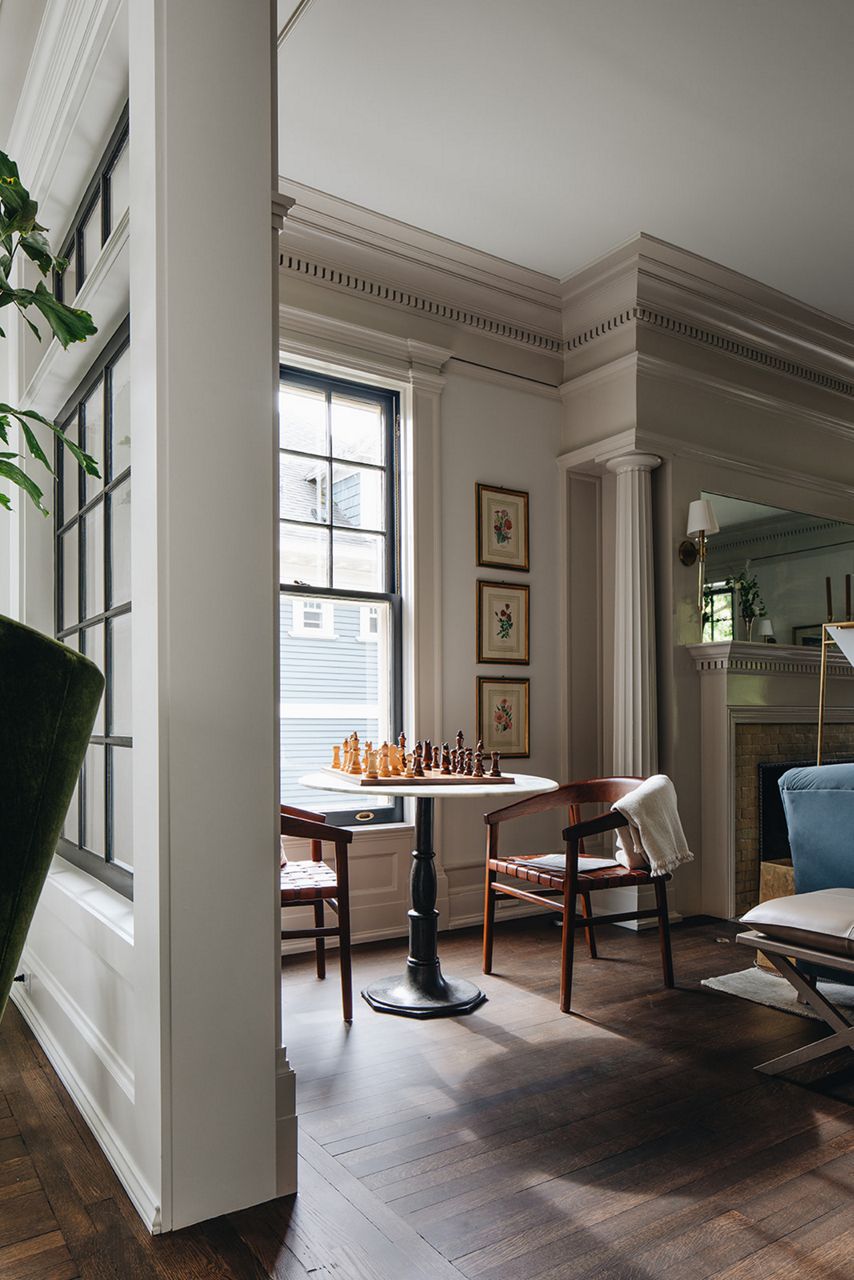 Two wooden dining chairs with curved backs sit at a white topped pedestal table with a chess board set for a game on top of it.