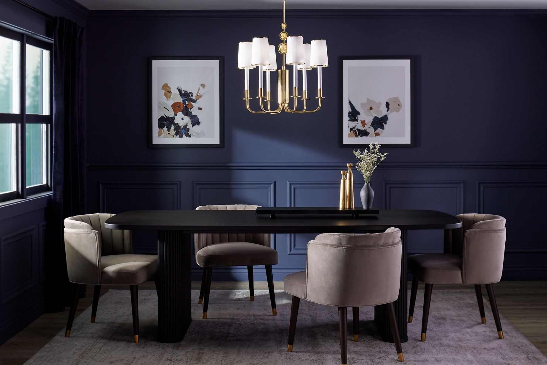 A six-light KOHLER Tresdoux chandelier hangs above a black oval dining table in a room with dark blue walls and large, framed floral prints.