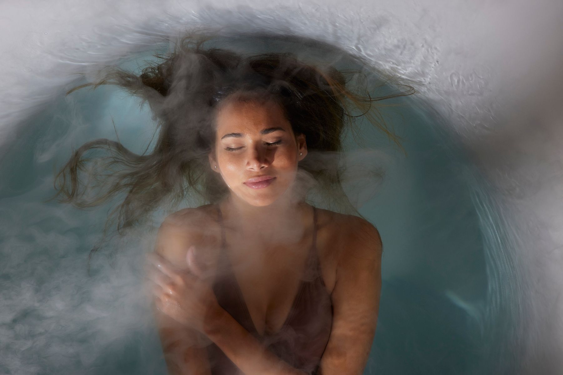 Woman relaxing in a bathtub filled with water and flowers, eyes closed in a tranquil setting.