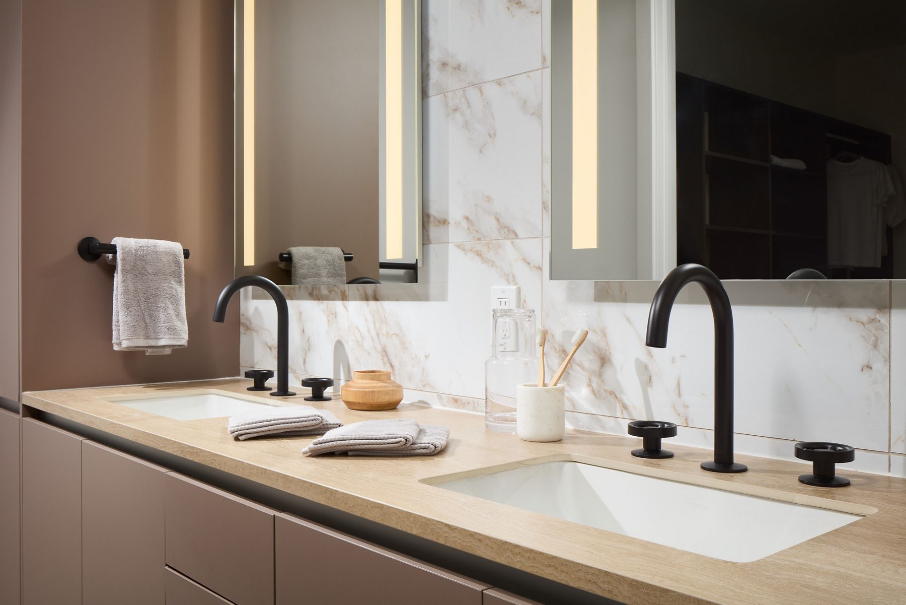Photo of bathroom sink area with double sink and luminated vanities fitted with Kohler faucets and handles in matte black.