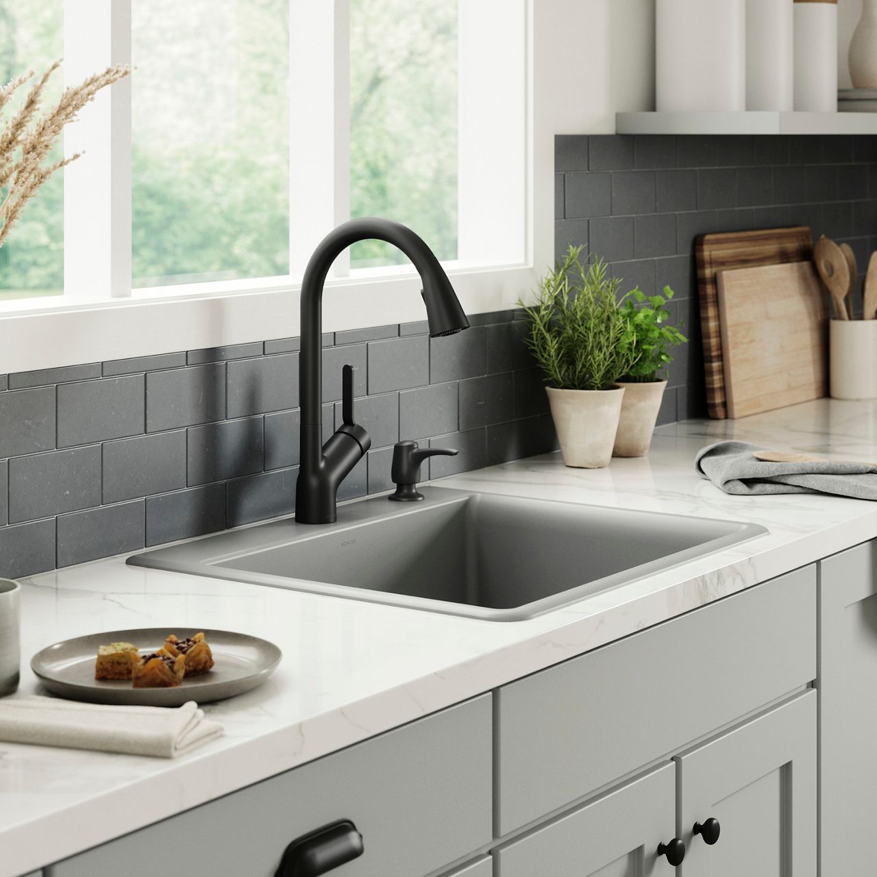Matte black pull-down kitchen faucet with a single-bowl sink beneath a bright window.