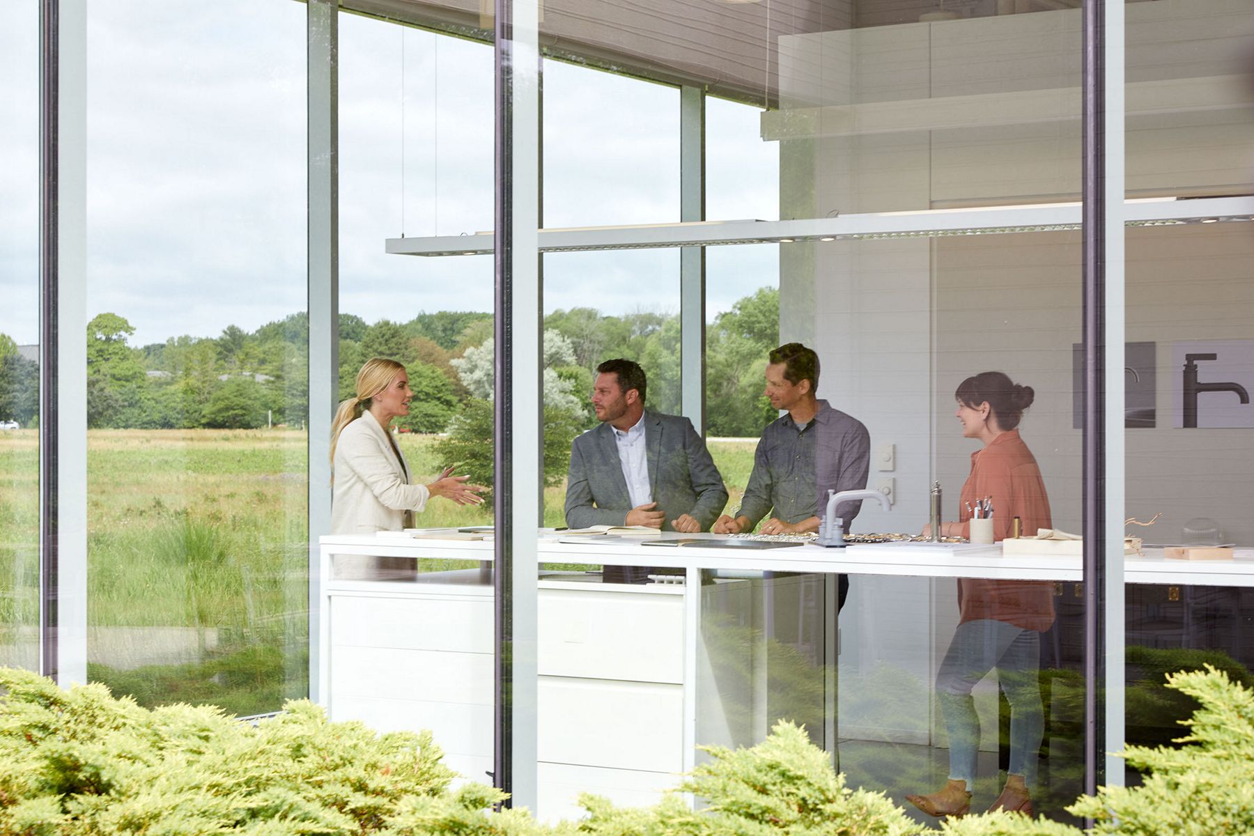 Designer Shea McGee in a glass walled room speaking at a tall white table with three other people.