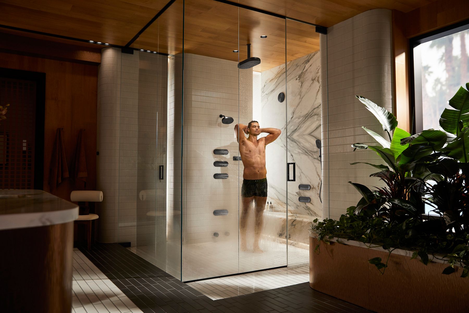 Man enjoying a full-body shower experience inside a luxury glass shower with multiple water outlets.