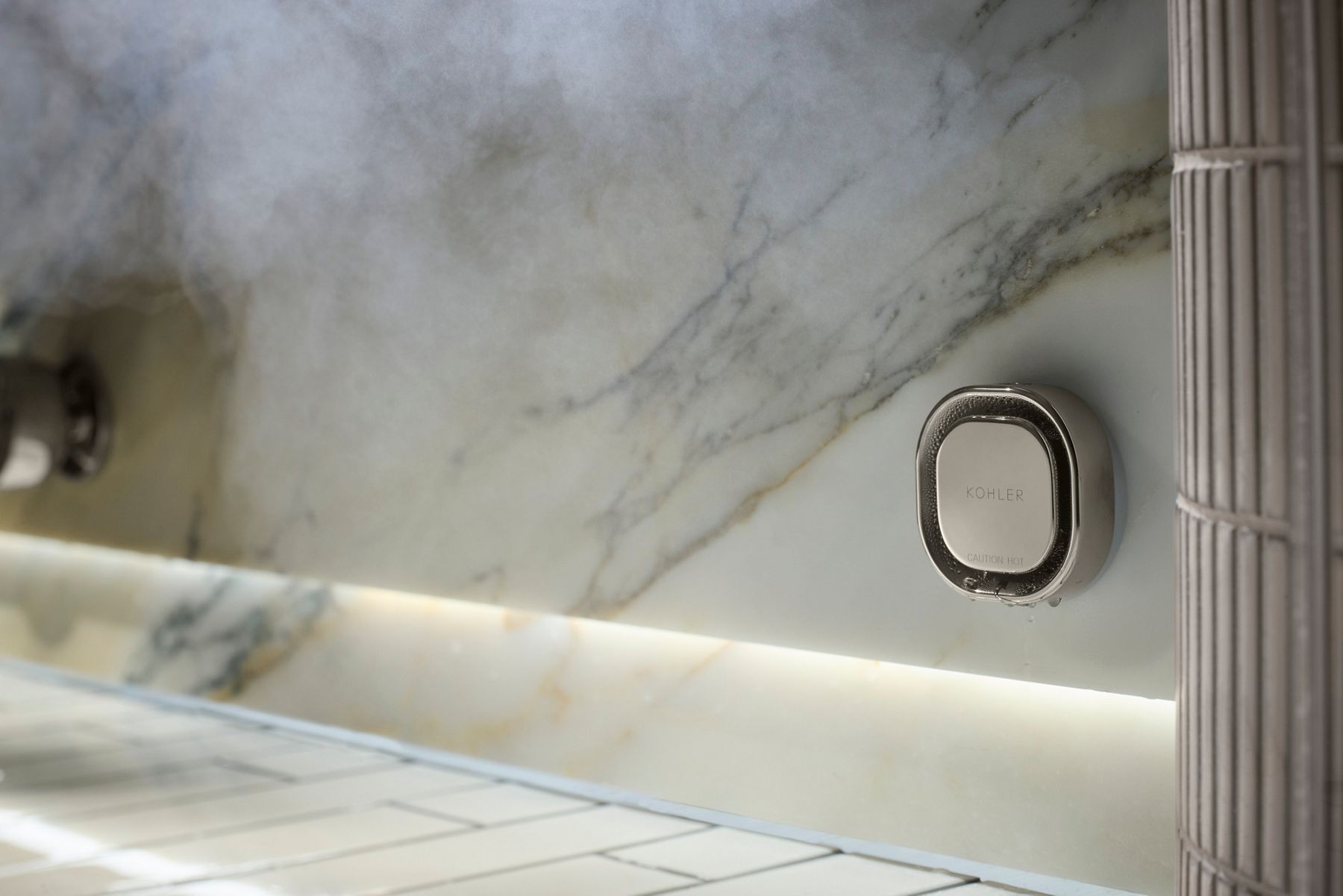 Close-up of a KOHLER digital steam shower device installed on a marble shower wall.