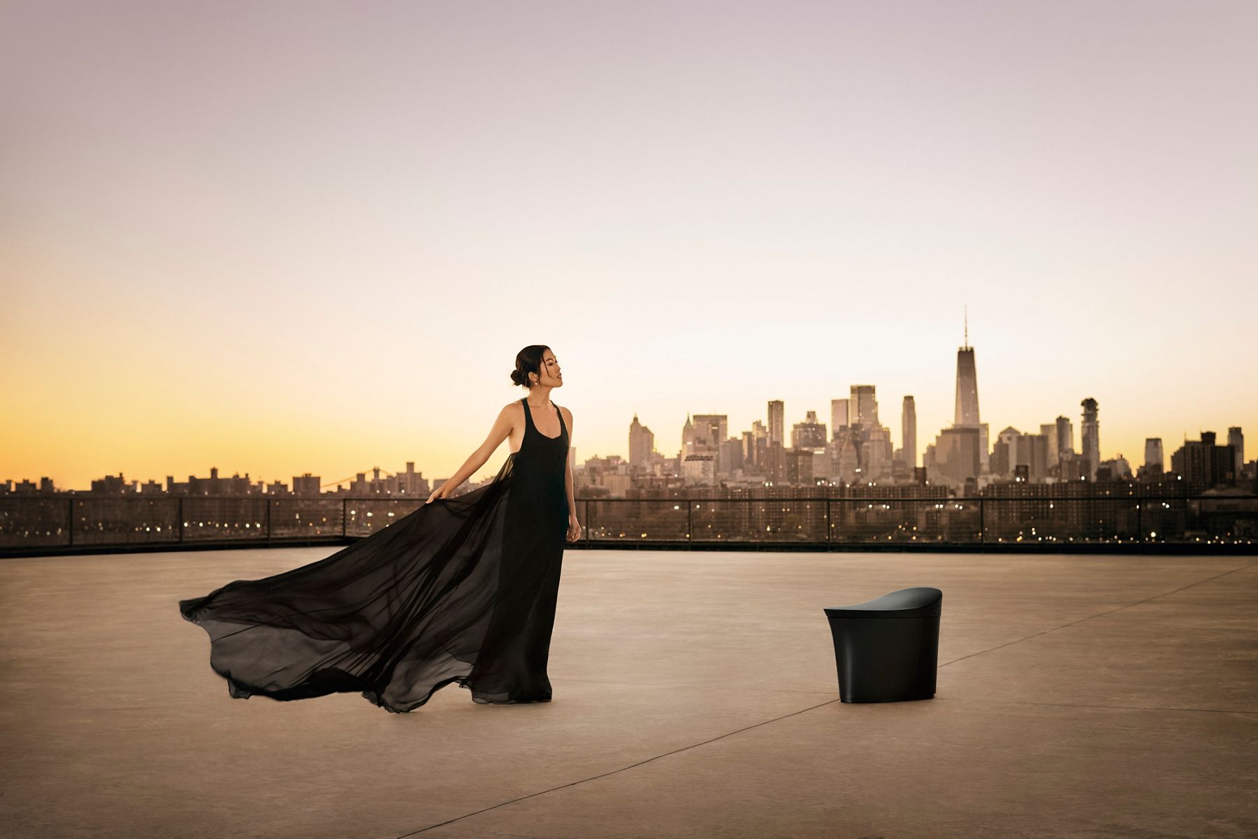 Laura Kim in flowing black dress standing on rooftop with New York City skyline in the background.