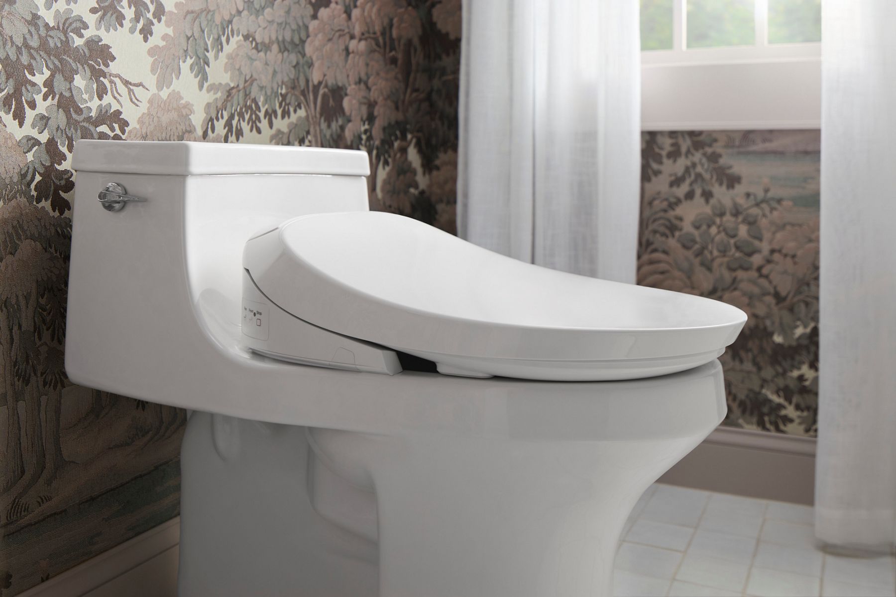 Bidet seat installed on a toilet with the lid closed, shown from a side view in a bathroom setting