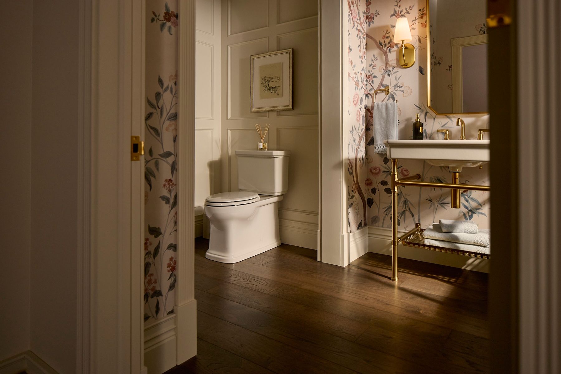 Elegantly designed, warm bathroom with floral wallpaper and natural afternoon light featuring a KOHLER Claude collection toilet and sink.