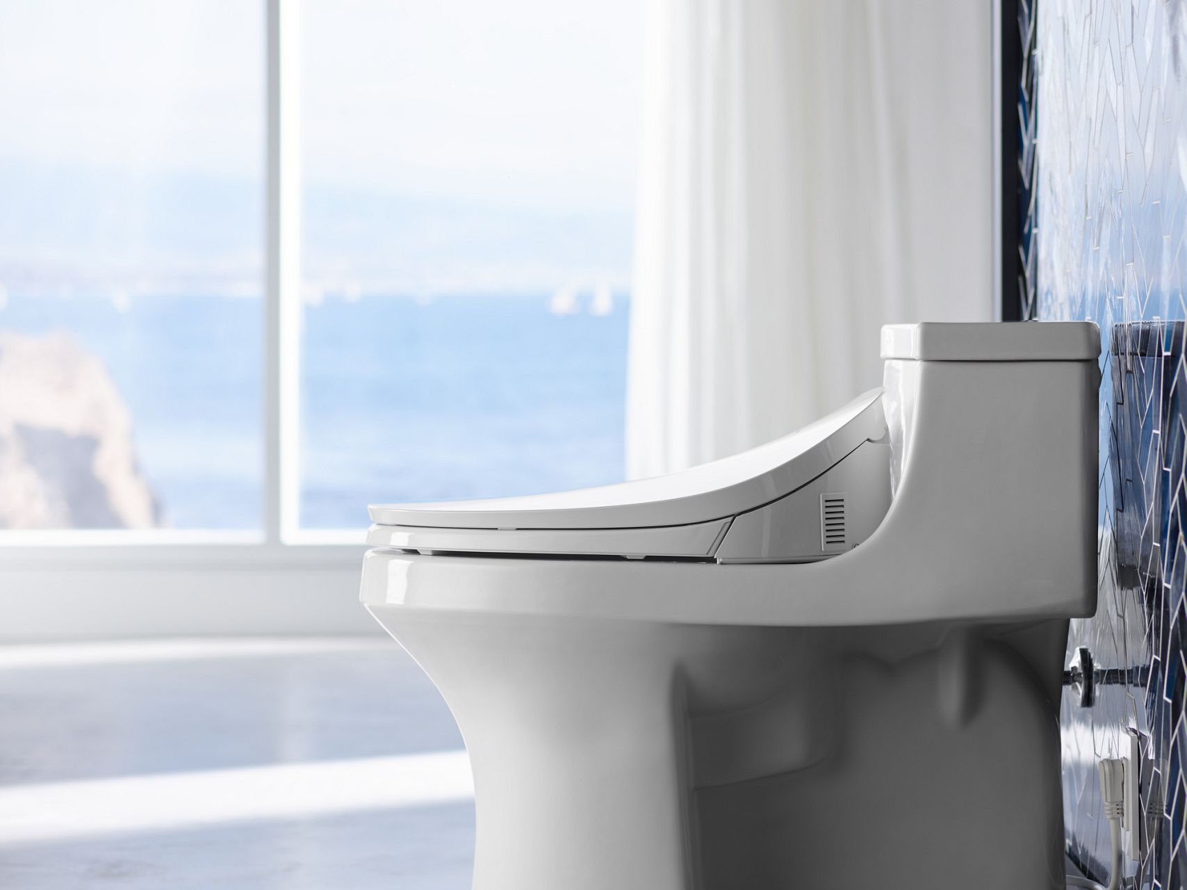 A white Kohler cleansing toilet seat with open lid, spray nozzle, and control panel.