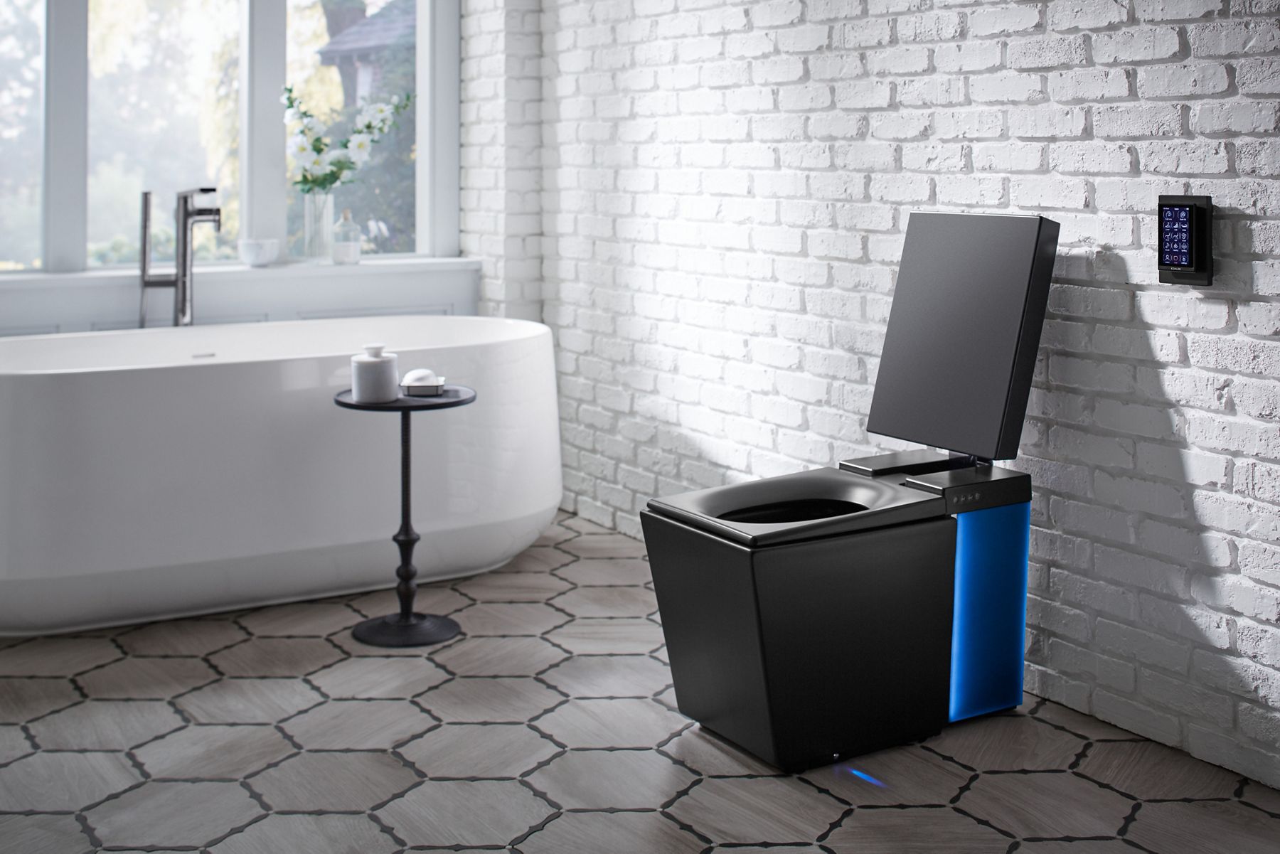 A contemporary bathroom with large hex floor tiles, black KOHLER(R) Numi Intelligent toilet, white brick walls and white freestanding bath.