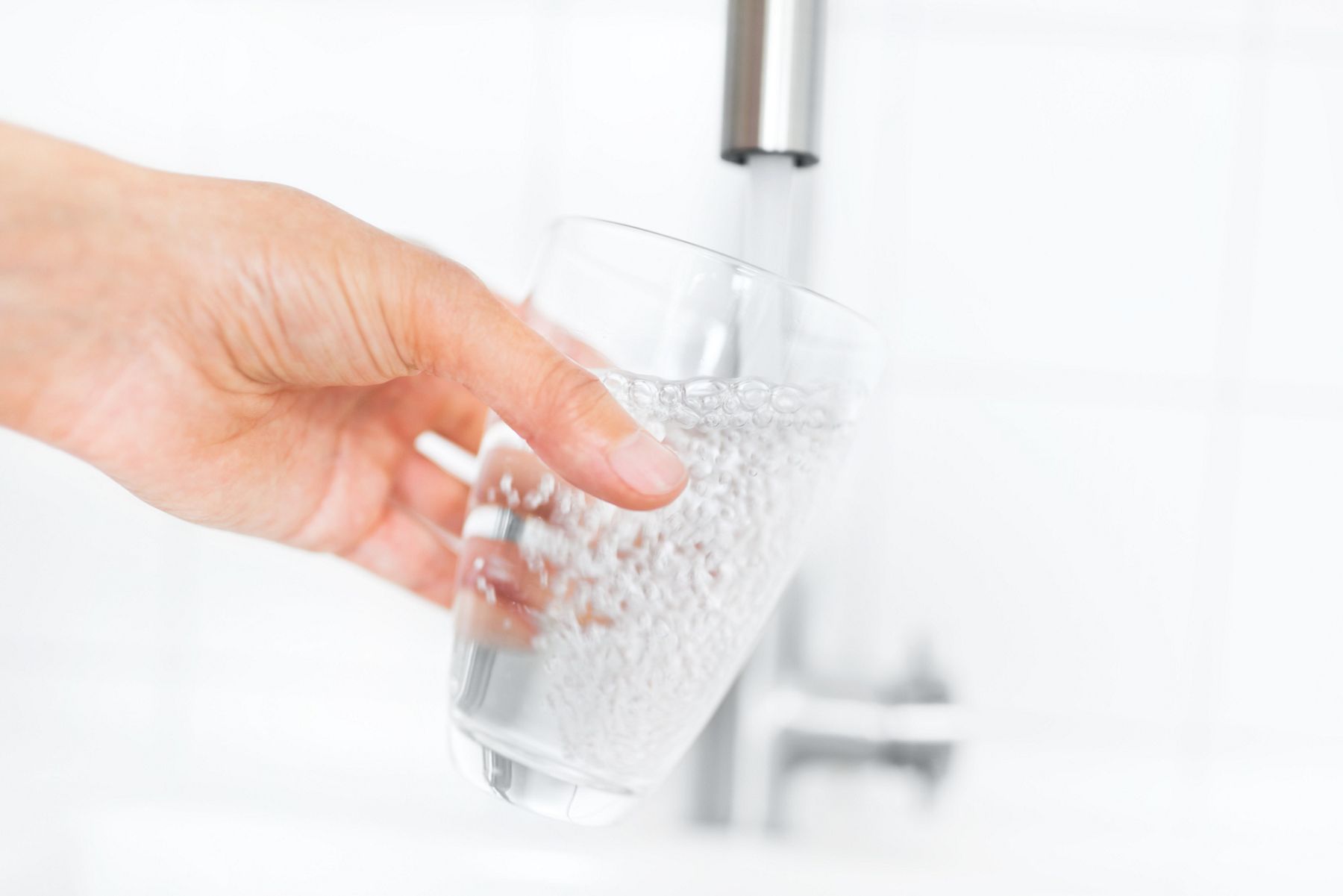 A person fills a glass with water from a faucet equipped with a KOHLER water filtration system.