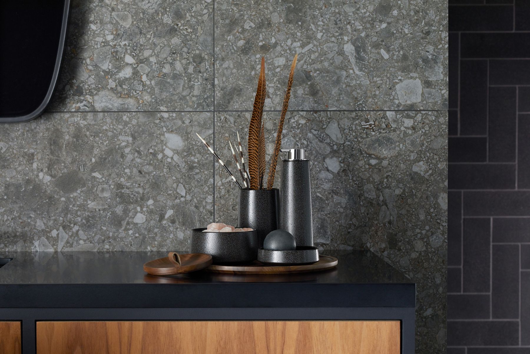 A black 4-piece Kohler bente accessory collection sits on a black countertop wood vanity in front of a dark marble wall.