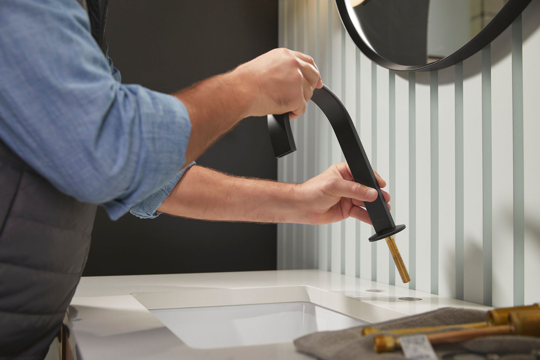 Person installing a matte black bathroom faucet onto a sink countertop.
