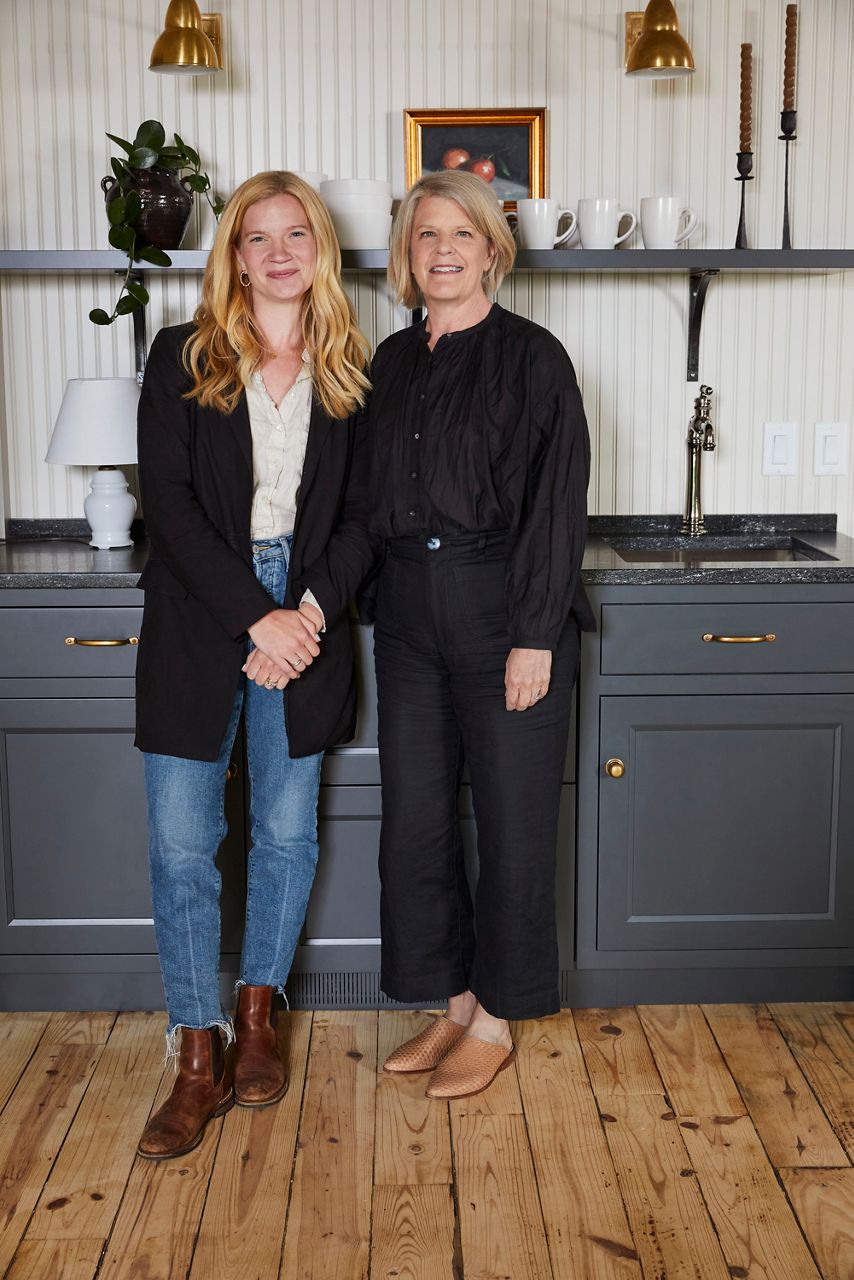 Portrait of Jean Stoffer and Grace Start, mother-daughter design partners, standing in front of the coffee bar at their newly renovated Michigan rental cabin.