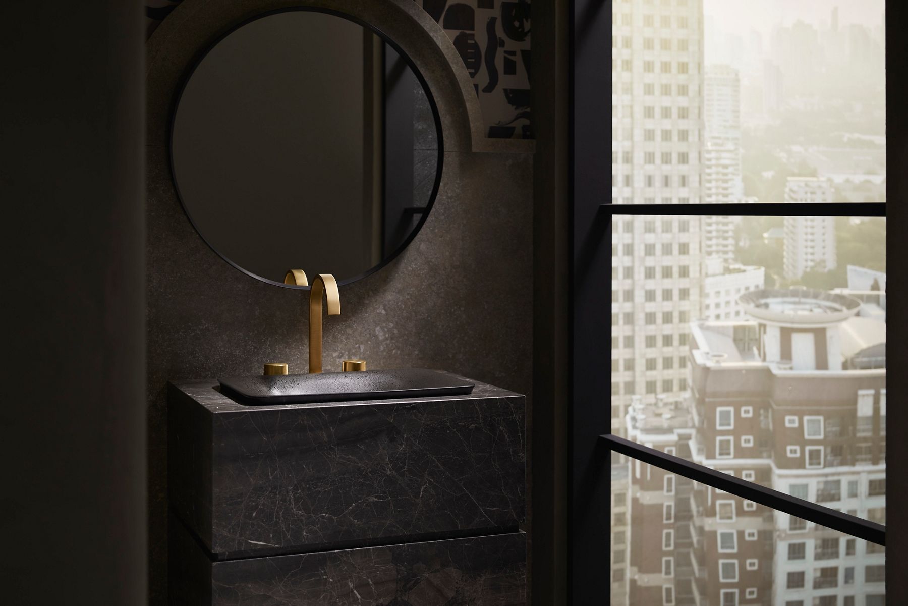 A bathroom vanity with a textured black rectangular drop in sink and modern brushed brass faucet on a dark gray stone vanity.