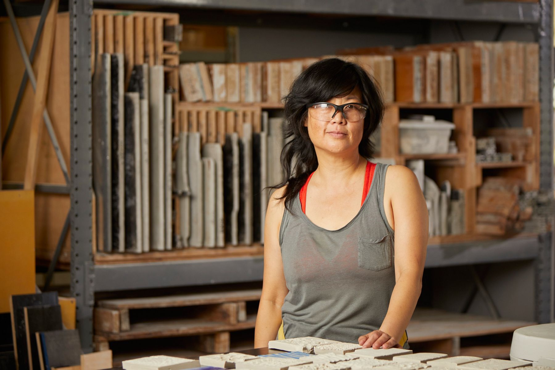 Artist Patty Chang standing in a ceramic studio surrounded by shelves of clay materials.