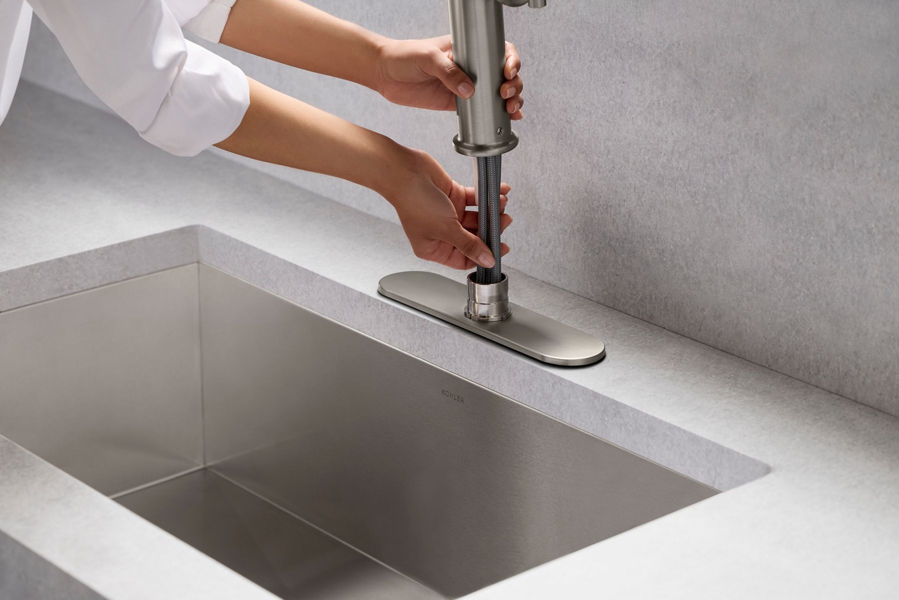 Hands installing a kitchen faucet into a white quartz countertop with an undermount stainless steel sink. Close-up view highlighting the faucet installation process and clean, contemporary design.