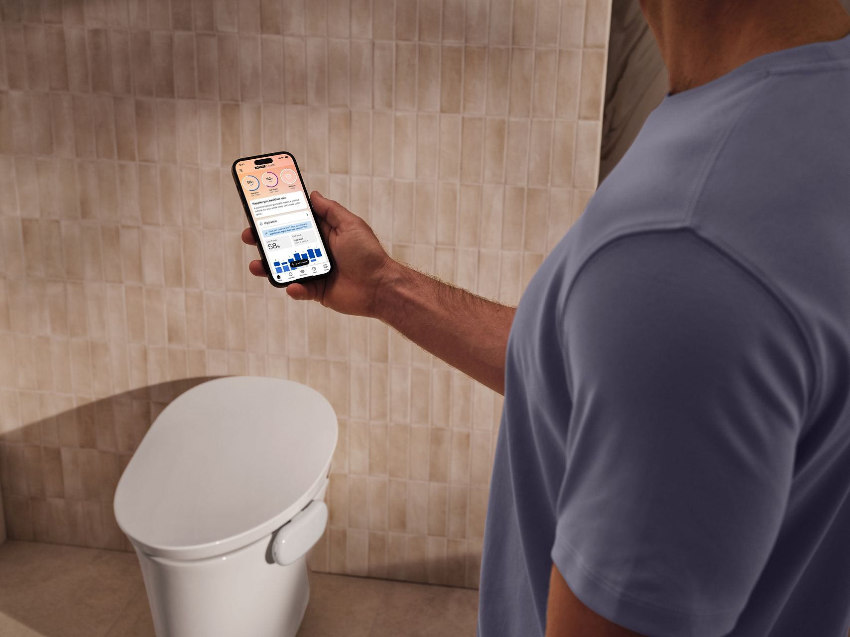 Hand holding a smartphone displaying the Kohler Health app dashboard with hydration, gut health, and wellness insights from Dekoda.