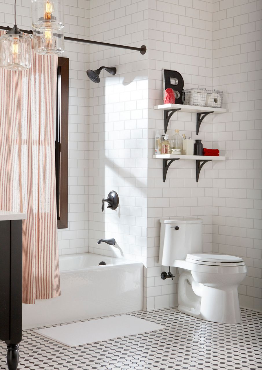 Glossy alcove bathtub in a bright, modern bathroom with white subway tile, black and white tile flooring, and an orange striped shower curtain.