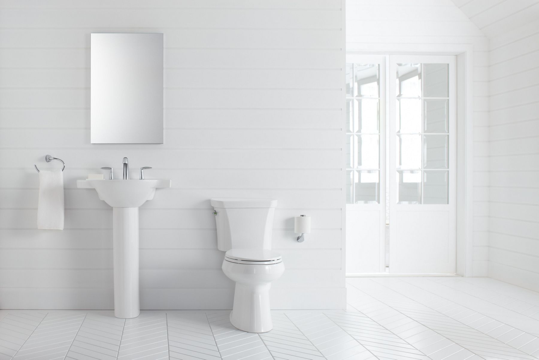 White bathroom with white pedestal sink and KOHLER Highline comfort height, dual-flush toilet.