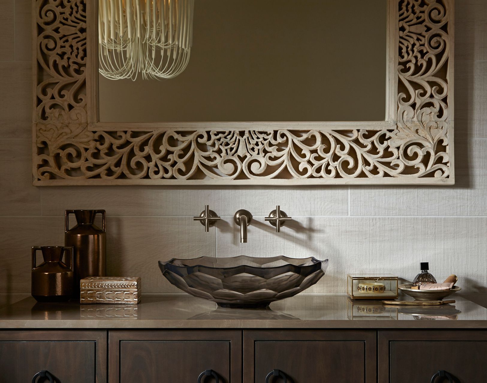 A bathroom vanity with a dark gray faceted glass vessel sink and a wall mount faucet on white tile.