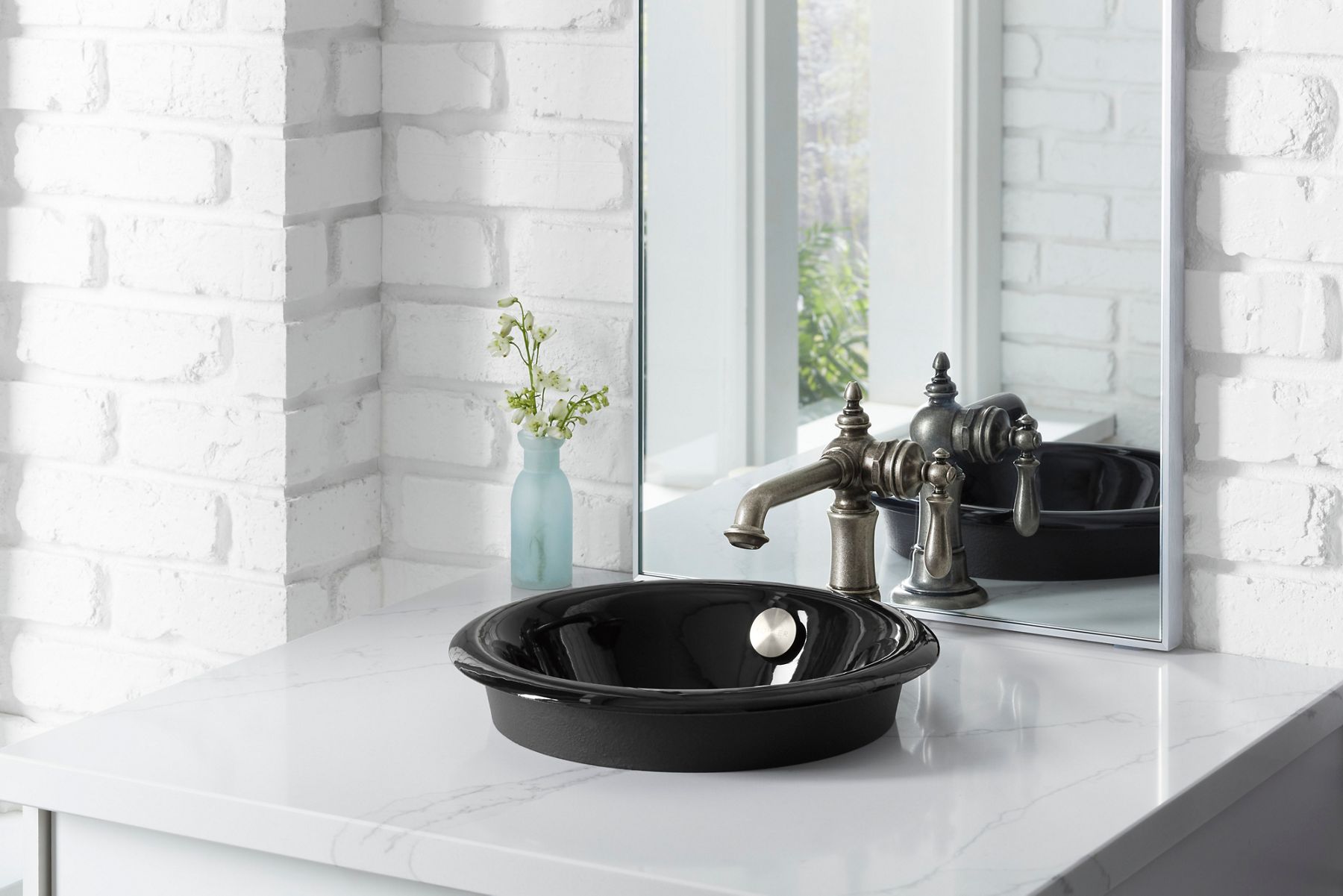 A glossy black drop-in sink on a white counter with a brushed bronze traditional faucet.