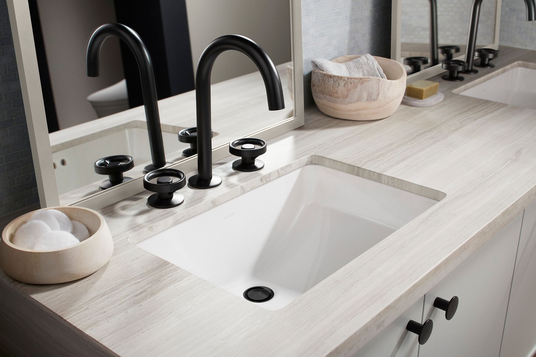 A bathroom vanity with a striated beige colored top, an undermount white sink, and a matte black contemporary faucet.