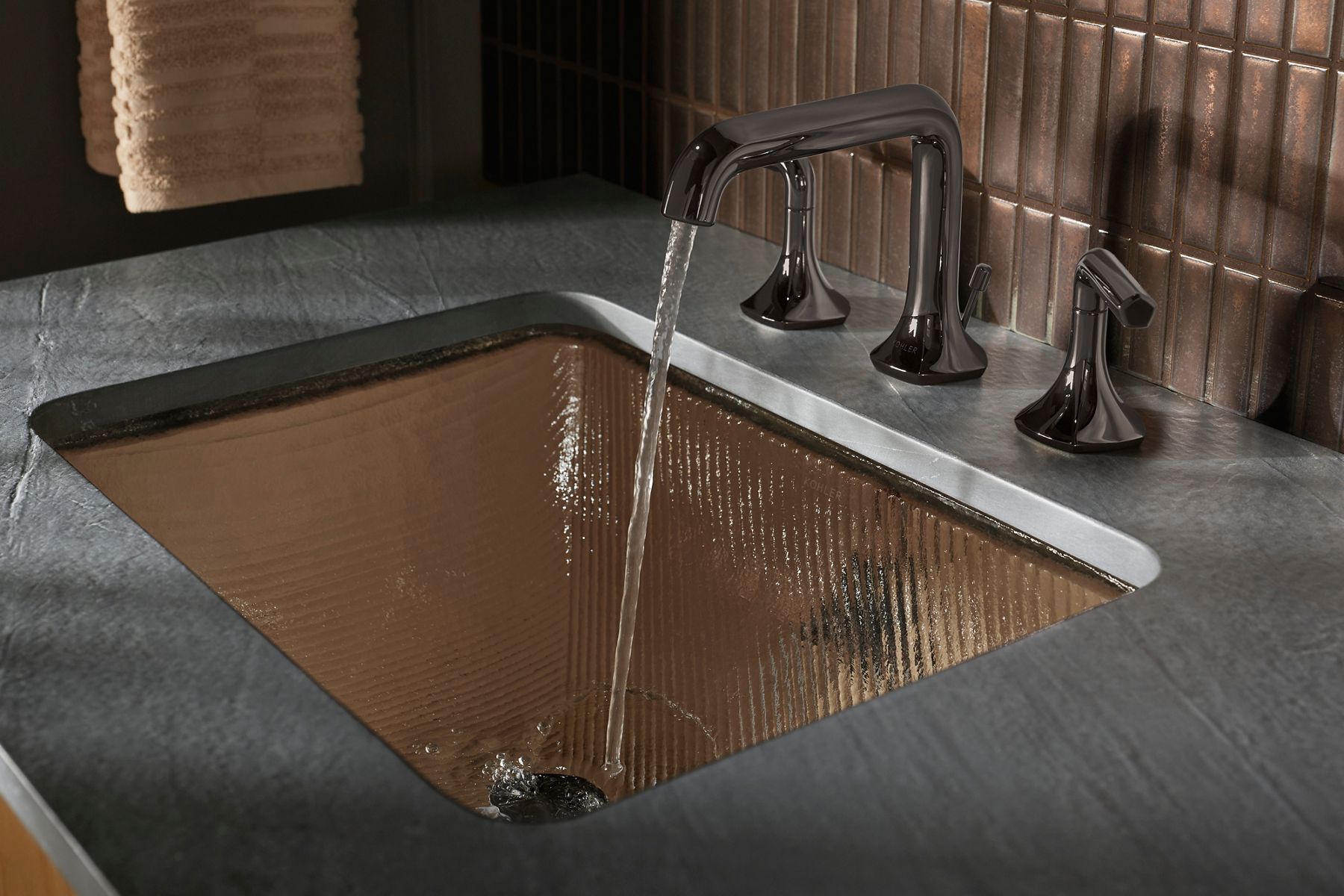 Water pouring into a ridged glass bathroom sink from a modern titanium finish faucet.