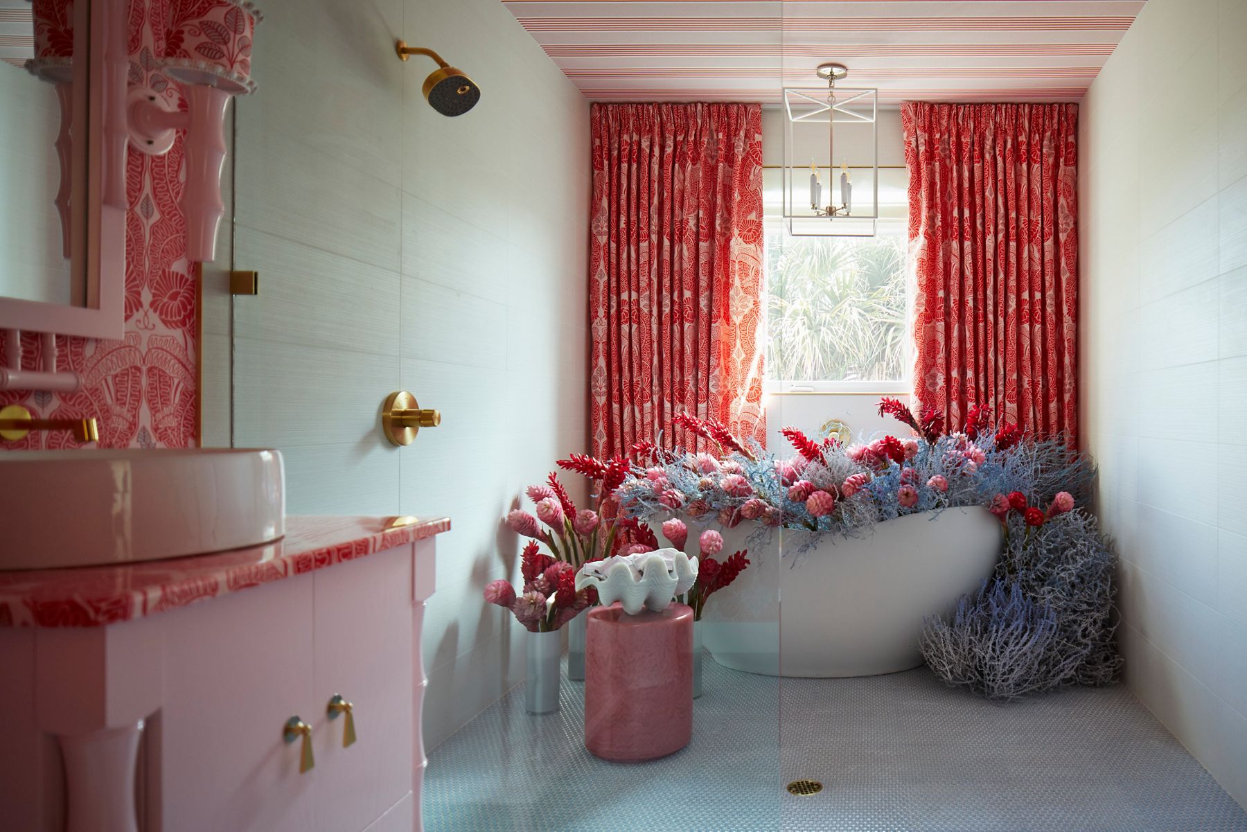 A bathroom in lush pinks and patterns with a freestanding bath filled with a floral arrangement.
