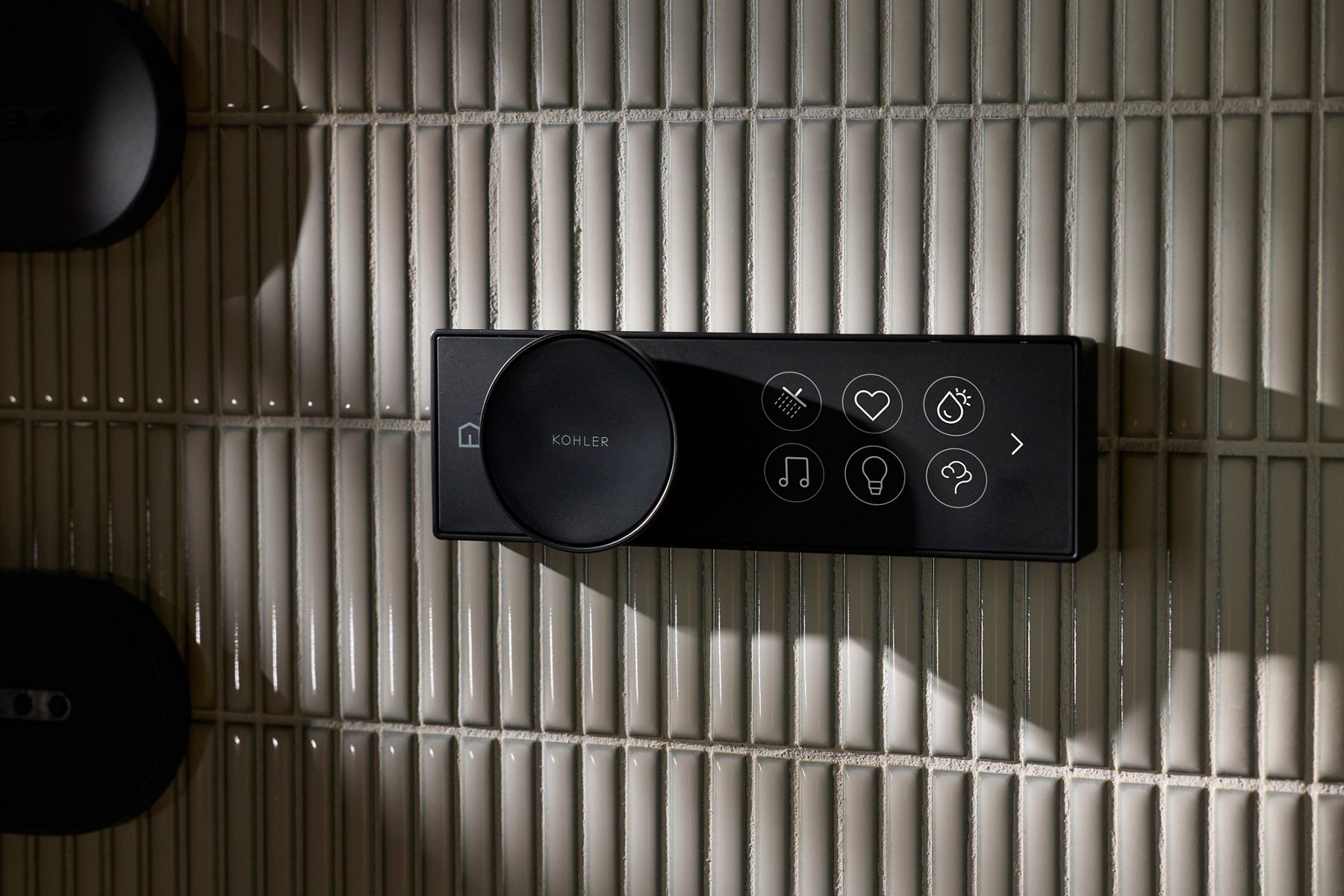 Kohler Anthem+ Ice Shower smart control panel with icons for water, heart, music, and temperature, mounted on tiled wall.