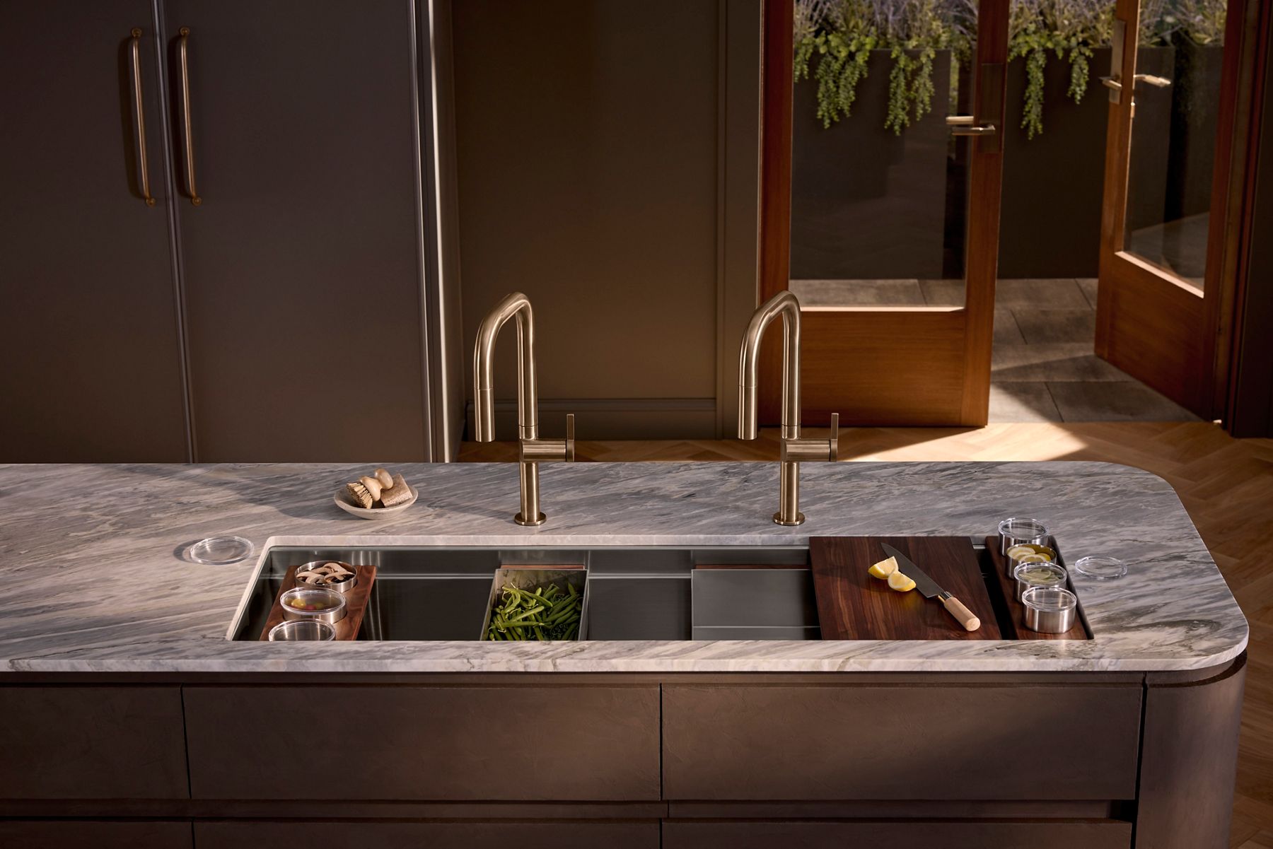 A Synthos™ Workstation sink a warm brown kitchen with arched gold faucets.