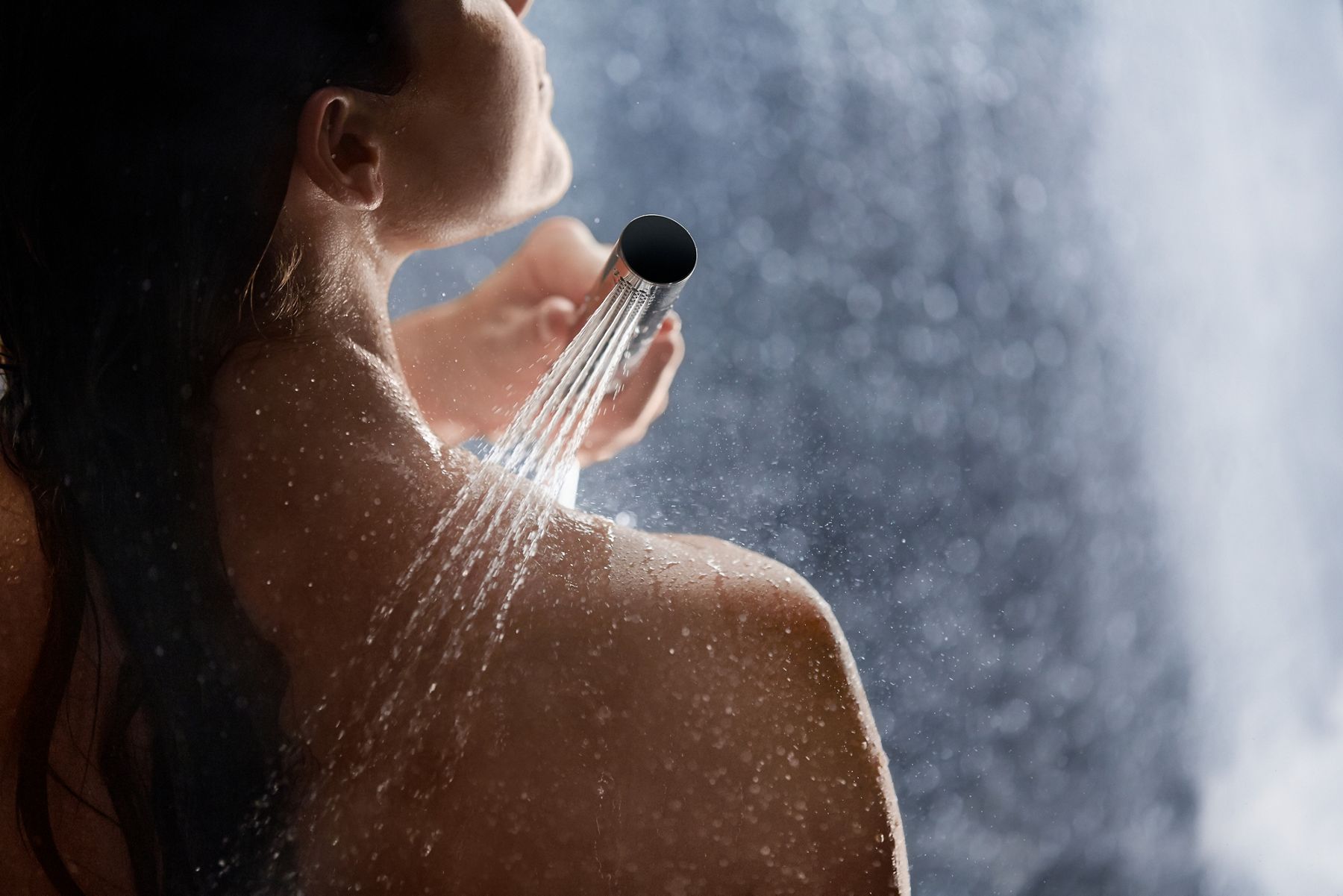 A woman uses a handshower to rinse soap from her shoulder.