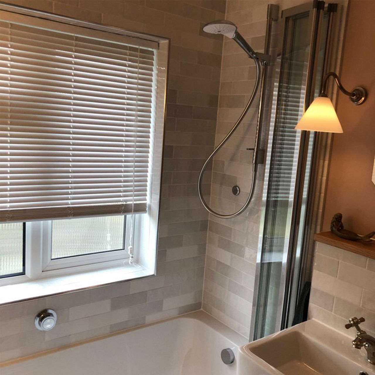 An after picture of @1930s_solo_renovation's renovated shower-over-bath area with natural toned tiles and a bifold shower screen.