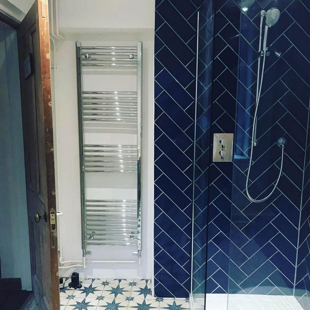 An after picture of @two_vets_and_a_wreck's renovated bathroom with a walk-in shower with blue herringbone tiles, floor tiles with stars and a large towel radiator.