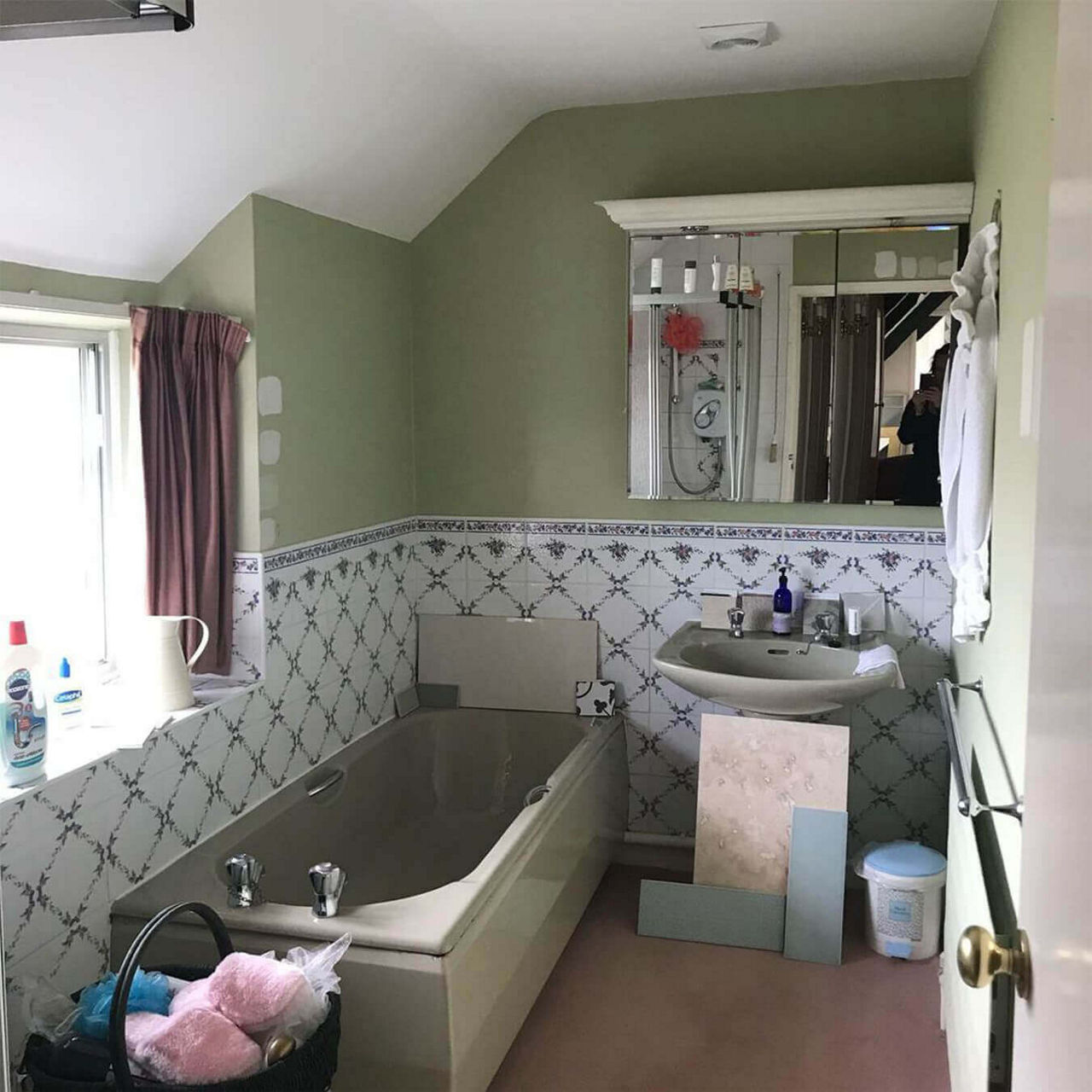 A before picture of @compton_randle's bathroom with a green bathtub, sink and top half of the walls, and white floral tiles on the bottom half.