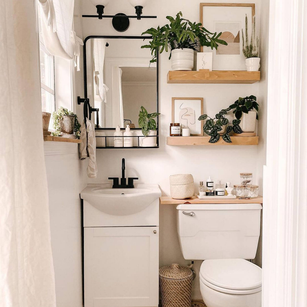 An after picture of @thistle.harvest's renovated white bathroom with wooden shelves and black fixtures on and above the toilet and sink.